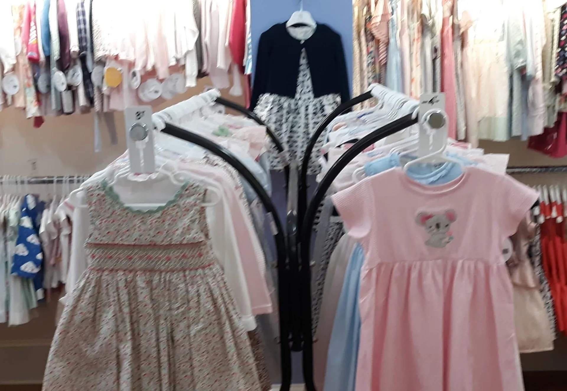 Rack of girls’ dresses at the boutique, including a smocked floral dress and a pink koala dress