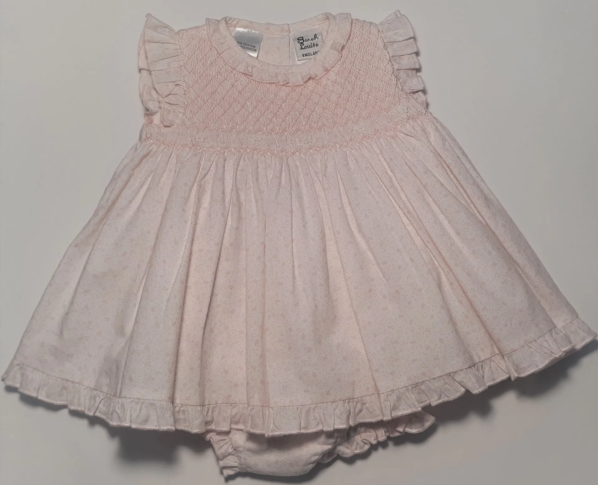 Pale pink smocked baby dress with ruffled sleeves and matching bloomers